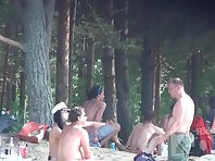 Nu1385#Nudist group took refuge from the sun in the shade of trees. They talk, have a drink 